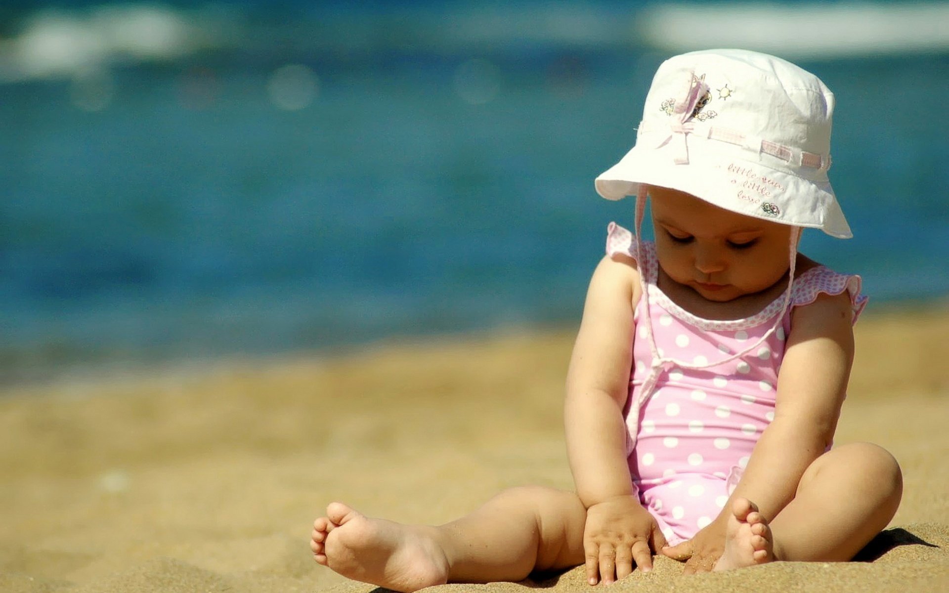 A little fashionista in a hat on the sand by the sea. Polka dot Swimsuit