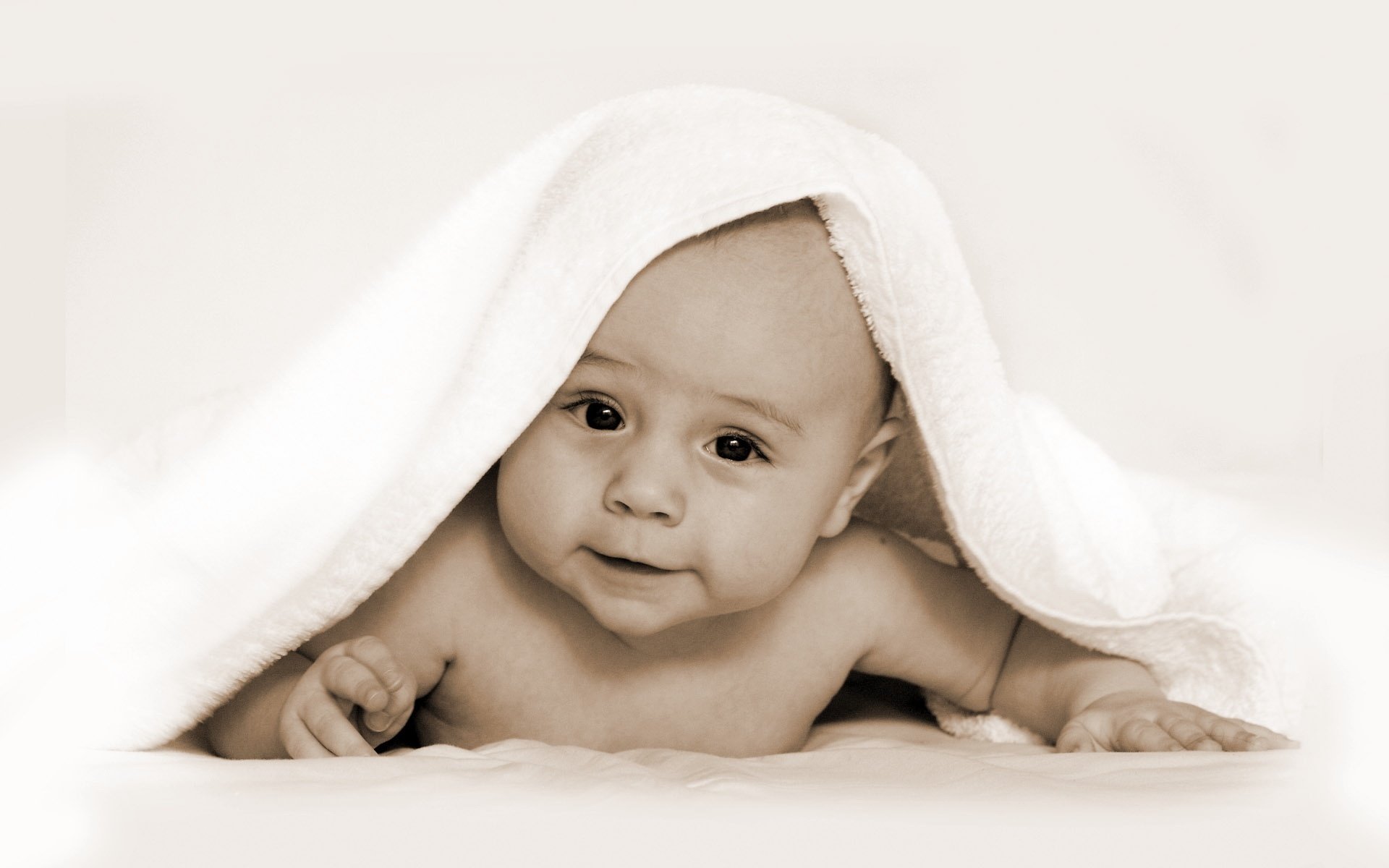 A baby lying on his stomach and peeking out from under a towel