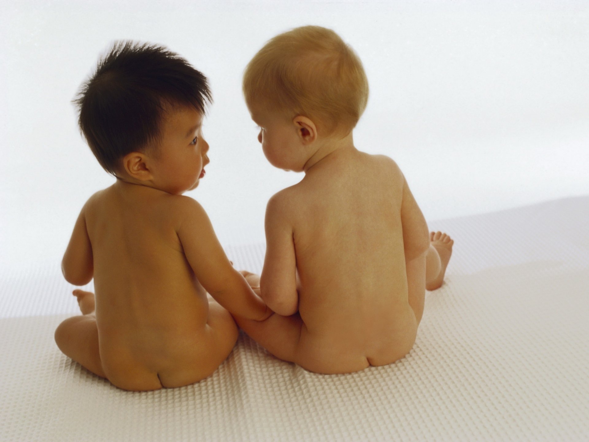 Two naked babies are sitting with their backs