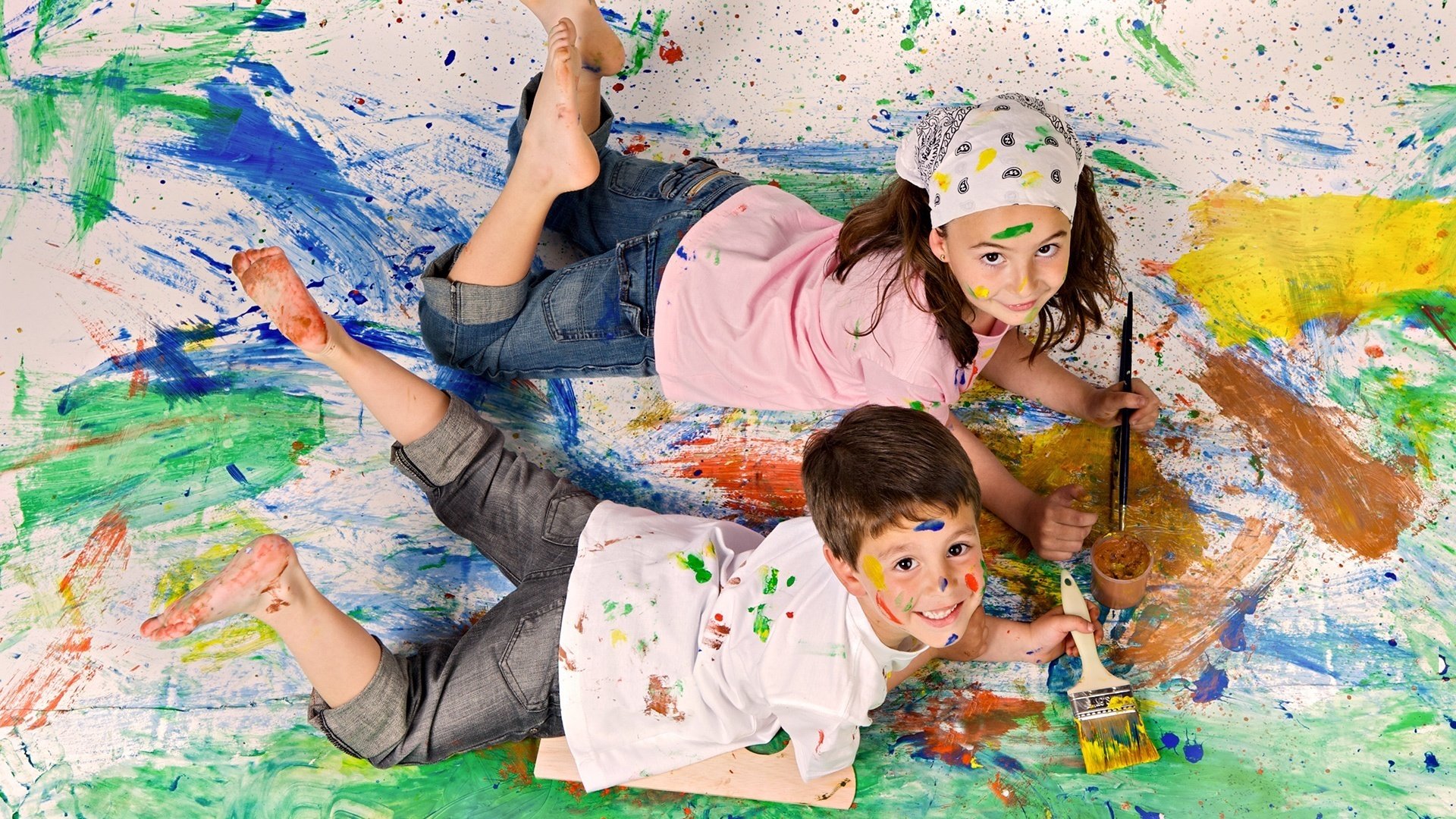 A boy and a girl paint with brushes on the canvas