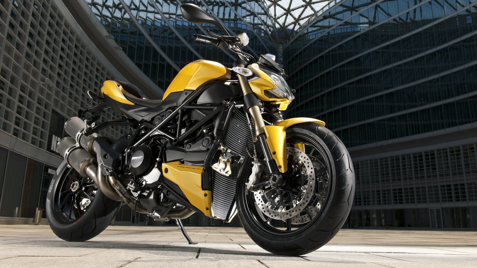 A yellow ducati streetfighter motorcycle stands on an urban background