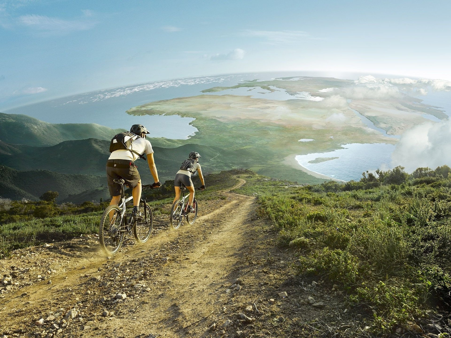 A married couple rides bicycles along green fields
