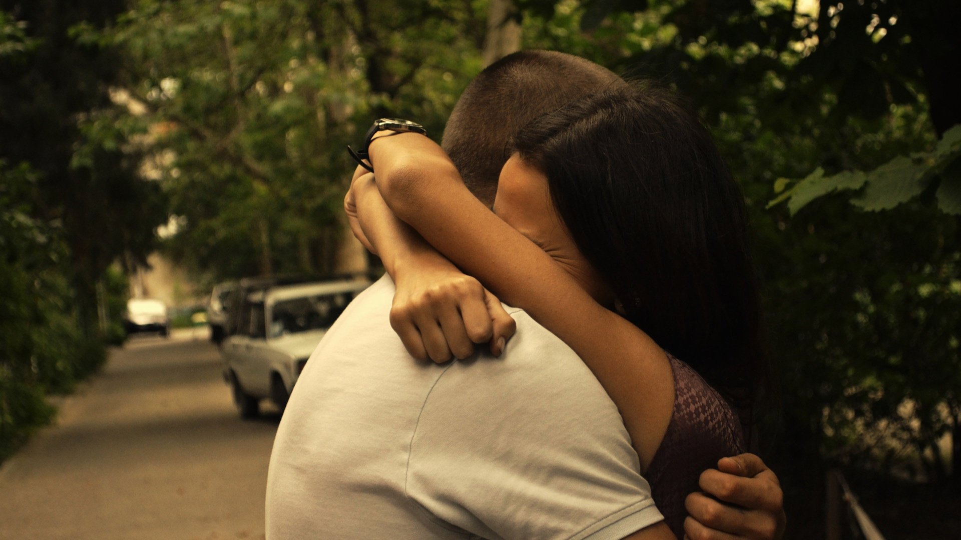 A woman and a man hug tightly among the trees