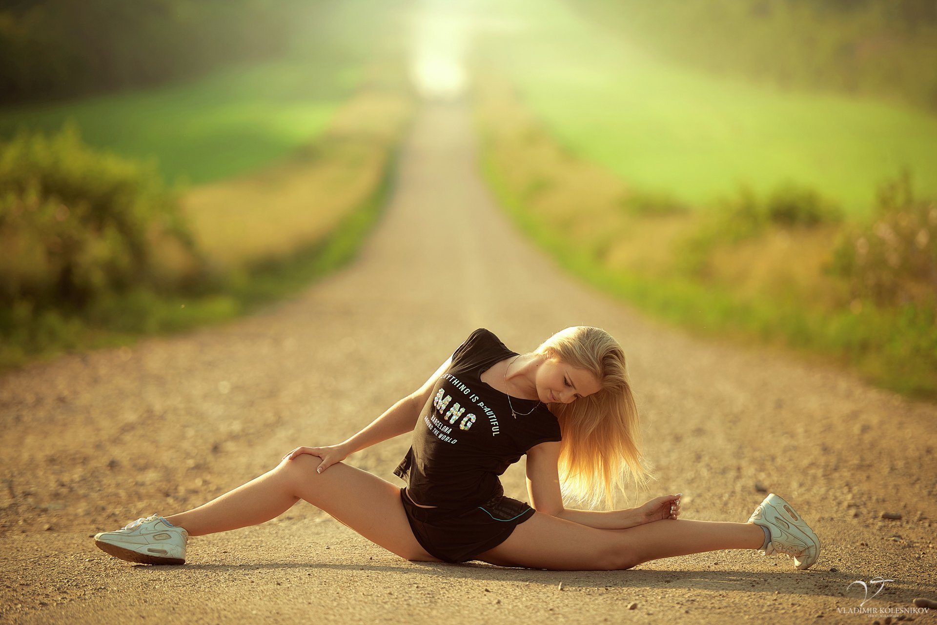 slim sports girl blonde village in the middle road pose stretching twine flexibility t-shirt shorts shoes sun green blur