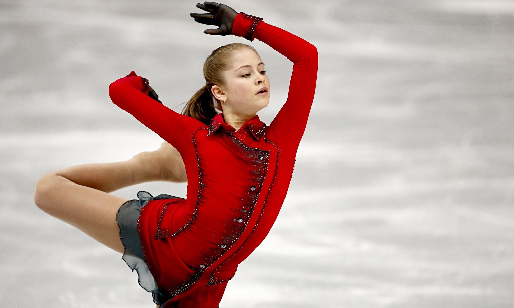 A figure skater in a bright, red suit rides on one leg