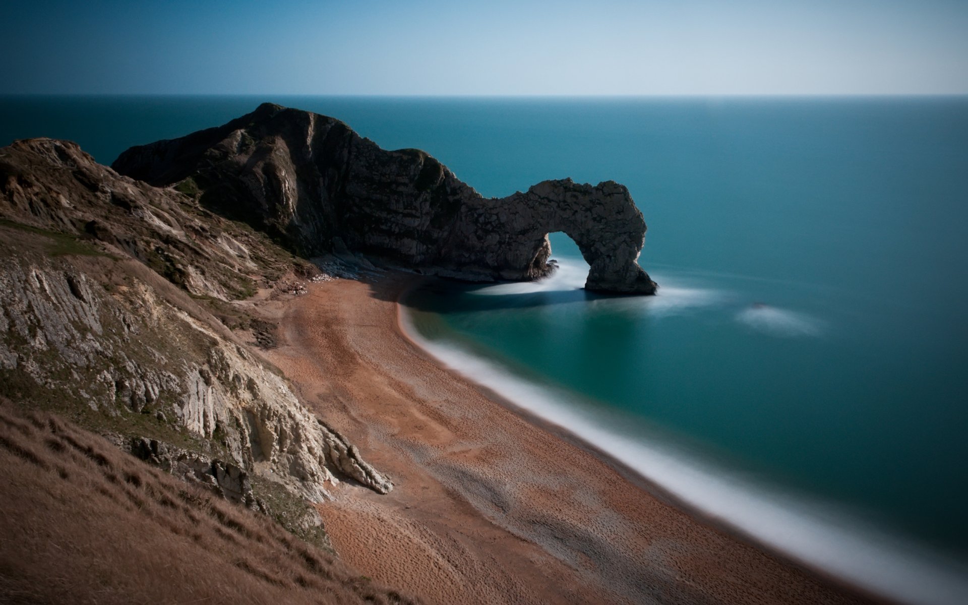 beautiful location arch triomphe beaches coast beach sand rock gates water ocean sea england britain united kingdom slopes hills grass stone stones photo scenery